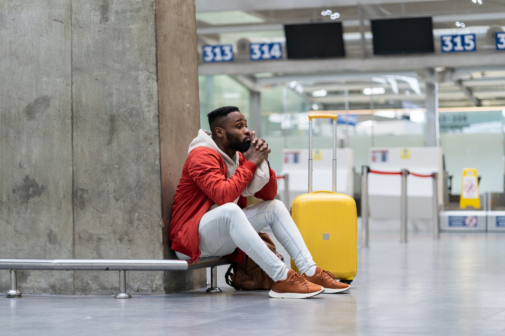 Tired Black tourist man on a long night connection at airport, waiting for plane sitting in terminal